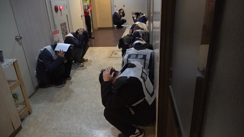 住民が屋内で身を守る姿勢をとる様子の写真