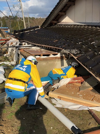 倒壊家屋の隙間から内部をうかがう千葉県警察本部職員の写真