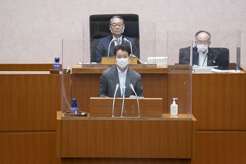 議場壇上議長席の信田議長と登壇し議案提案理由を説明する熊谷知事