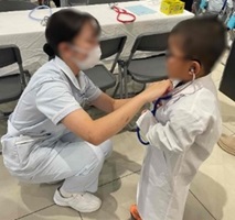 聴診器を体験する子どもと、サポートする生徒の写真