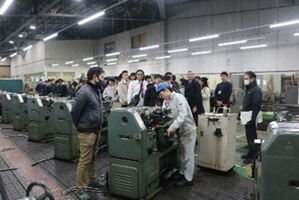 旋盤作業を行う千葉工業高校の生徒の様子を見学する東勢工の教員・生徒の写真