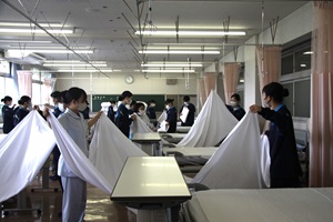 生徒が2人1組でシーツの畳み方を練習する様子