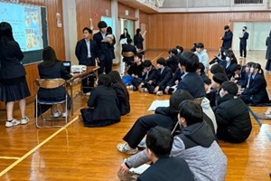 黒板の前で研究成果を発表する3年生3名と、説明を聞く後輩たちの写真