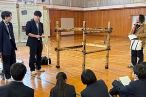 製作した木製模型を披露する3年生2名と、それを眺める後輩や地域の方の写真