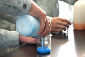 生徒が青色に着色したアルギン酸ナトリウム溶液をビーカーに注いでいる手元の写真