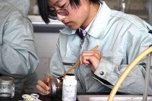 筆を使ってガラス瓶に薬品を塗っている生徒の写真