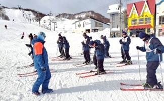 スキー板を履き、インストラクターから説明を受けている生徒たちの写真