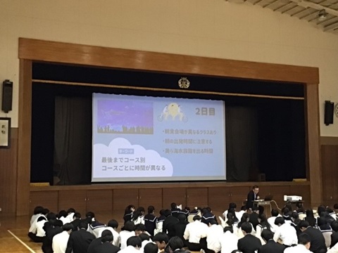 体育館のスクリーンを眺める生徒の写真