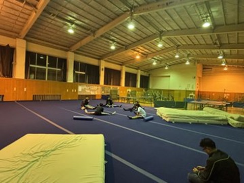 体育館に敷いた体操用マットでストレッチをおこなう生徒の写真