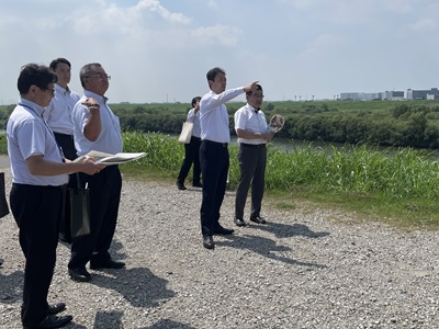 主要地方道越谷野田線野田橋周辺における現地視察の際、野田橋の方向を指さしながら市長の説明を聞く知事の画像