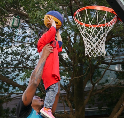 大人が子どもを持ち上げ子どもがバスケットゴールにシュートをしようとする写真