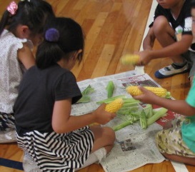 小学生がとうもろこしの皮むきをしている