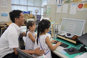 パソコンの前でお父さんと一緒に名刺を作る姉妹の写真