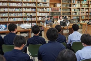 本棚を背景に話をするきゃんさんと五十嵐さんと、話を聞く生徒たちのの後ろ姿の写真