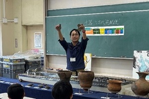 文化財課職員が教室で土器を手に持って開設している写真