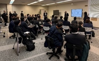 モニターの前で説明する生徒2名と、発表を聞く生徒たちの写真