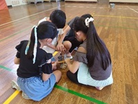 体育館の床に座って火起こしに挑戦する児童生徒たちの写真