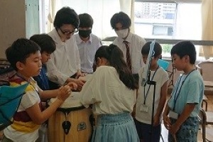 楽器のまわりに高校生と小学生がいる写真