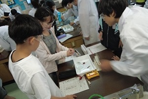 生徒1人が児童2人と一緒に安全に実験を行うための注意を確認している写真