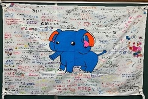 千葉聾学校のデフリンピック応援オリジナルキャラクター「ミミゾウ君」の周りに子供たちが寄せ書きした応援旗の写真