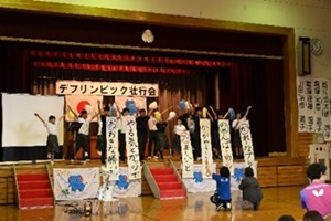 中学部生徒たちが、選手の頭文字を使い激励の言葉を筆で描いた作品を舞台上で披露している写真