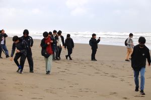 九十九里浜を歩く生徒と保護者たちの写真