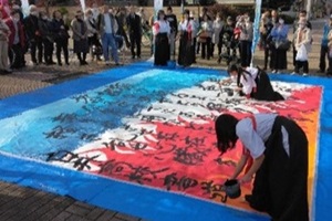 地面に置かれた大きな半紙に文字を書いていく書道部員たちの写真