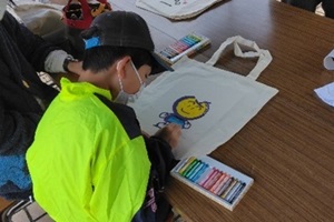トートバッグに書かれた「なし坊」に色を塗る子どもの写真