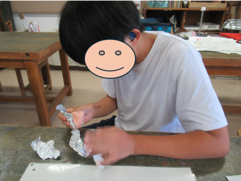生徒が紙粘土をアルミホイルに包んでいる様子