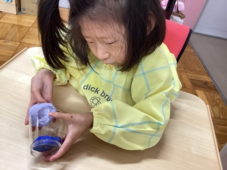 小学部女子児童が紫の紙粘土を入れているところ