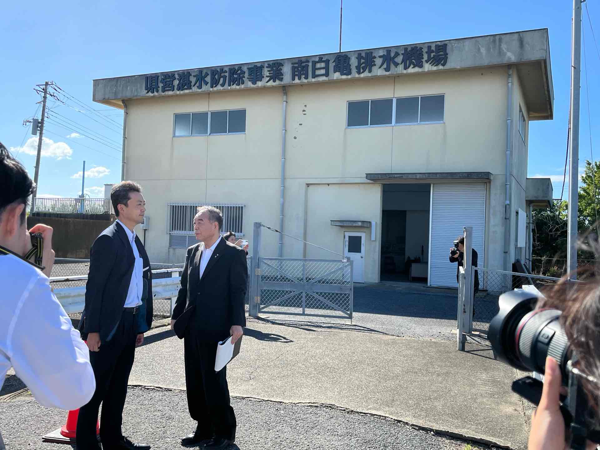 南白亀排水機場における現地視察の際、建屋の前で町長の説明を聞く知事の画像